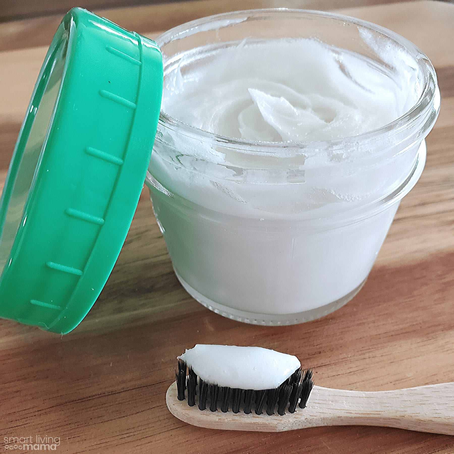 small jar filled with natural, homemade coconut oil toothpaste sitting on the counter and a toothbrush with toothpaste on it next to the jar